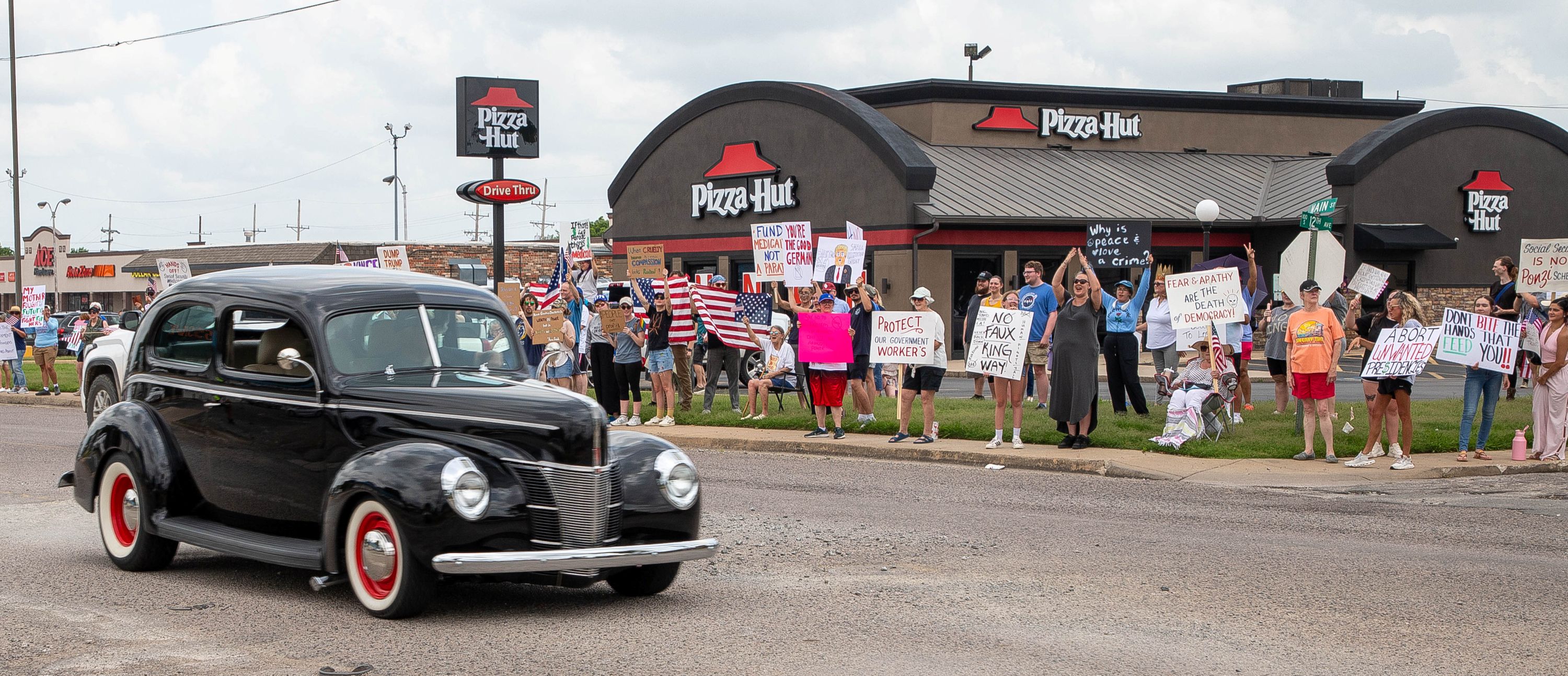 An antique car from the Draggin’ Main Car Show cruises past protesters on Saturday. 