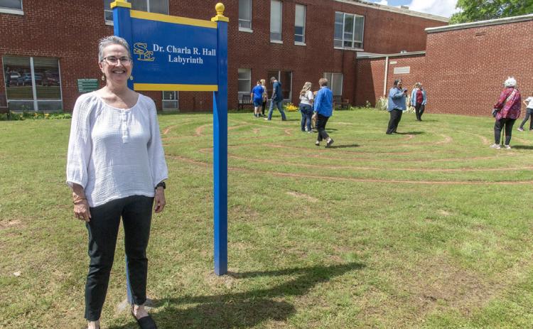 Dr. Charla R. Hall poses with the sign at the newly dedicated labyrinth, while community members walk the labyrinth. Dan Hoke | SE