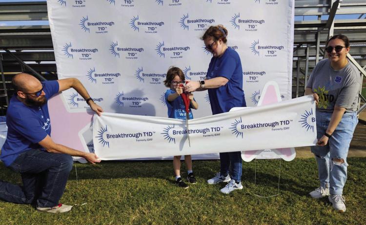 Seven-year-old Rhett Brewer, who was diagnosed with Type 1 diabetes when he was 5, cuts the ribbon before the Breakthrough T1D walk at the Durant Multi-Sports Complex to raise money for diabetes research. Organizers said more than $4,000 was raised. Also shown are Brewer’s parents, Ryan and Melissa Brewer, and Paris Al-Khateib. Matt Swearengin | Durant Democrat