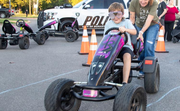 Rever Stephens rides a go-cart during the Durant Police Department National Night Out and also shown is his mother, Becca Dunegan.